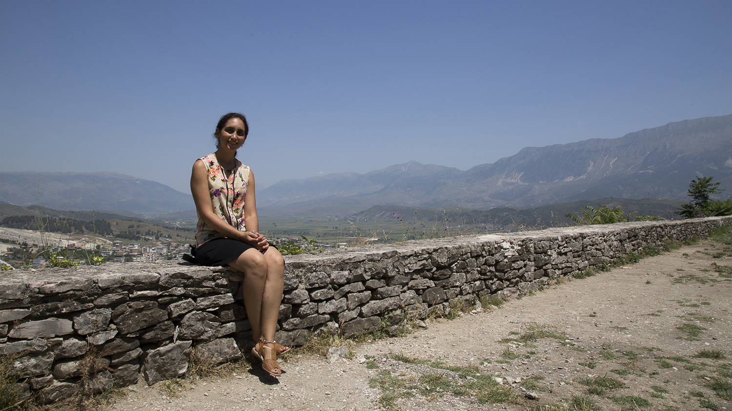 A student poses for a photo in Kosovo, on a brick wall.