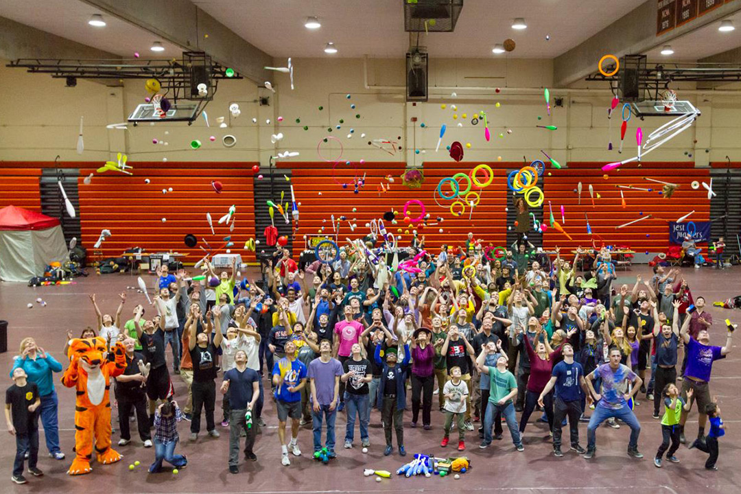 Large group of people throws juggling pins, hoops and balls into the air.