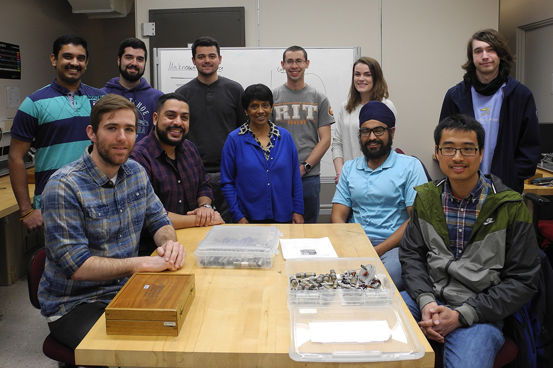 Group of students and researchers sit and stand around table.