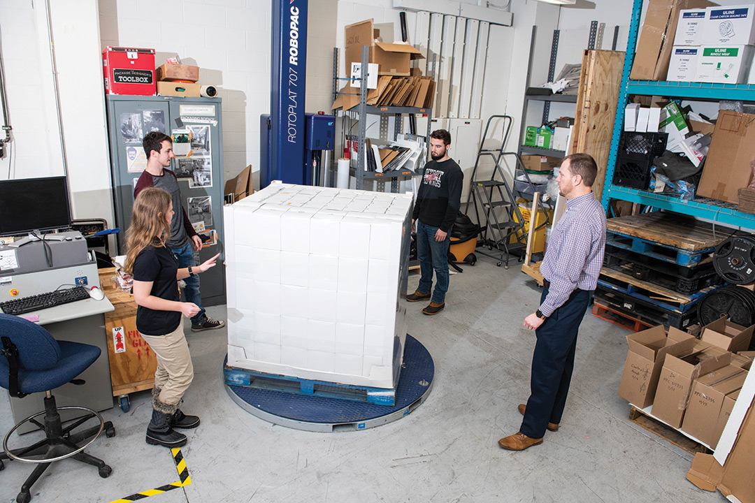 Students and professor stand around pallet with boxes.