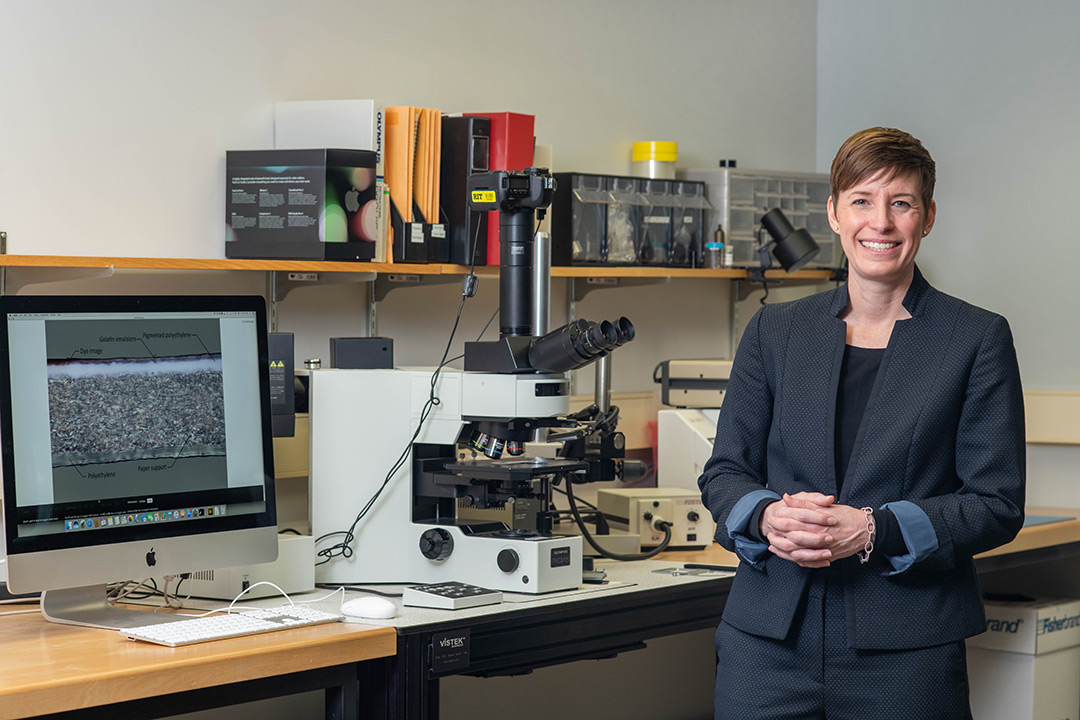 Woman stands next to desk with microscope and computer.