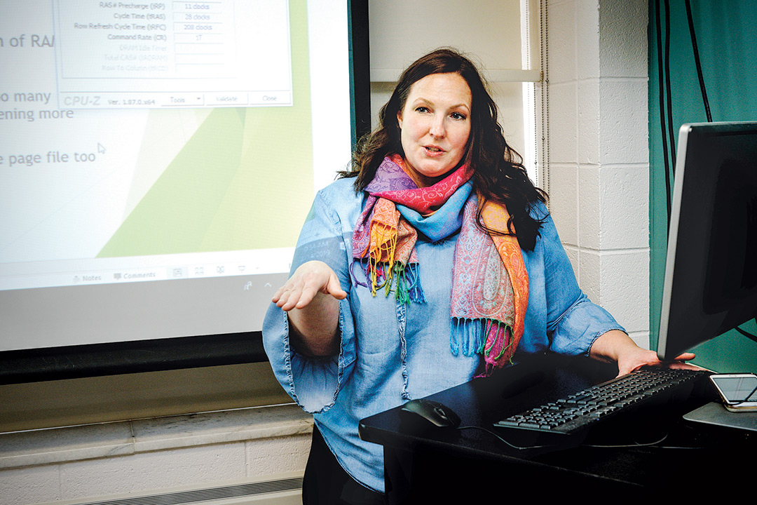 Woman stand behind computer and in front of projector screen.