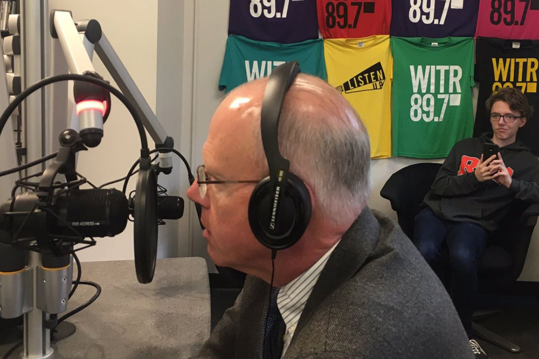 Man wearing headset speaks into radio station microphone.