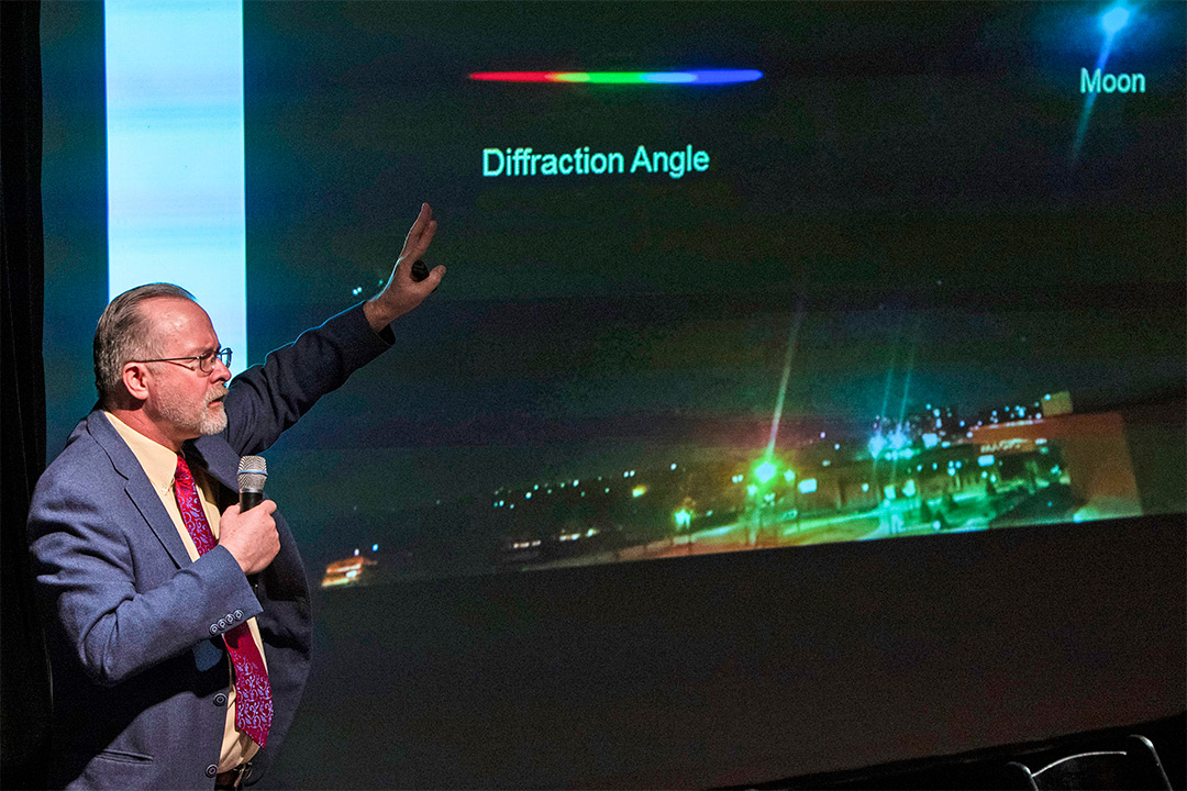 Man in suit gestures toward presentation.