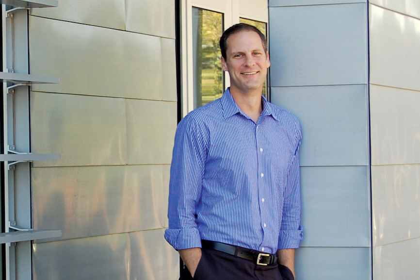 Man wearing blue striped button-up shirt stands against pillar outside of building