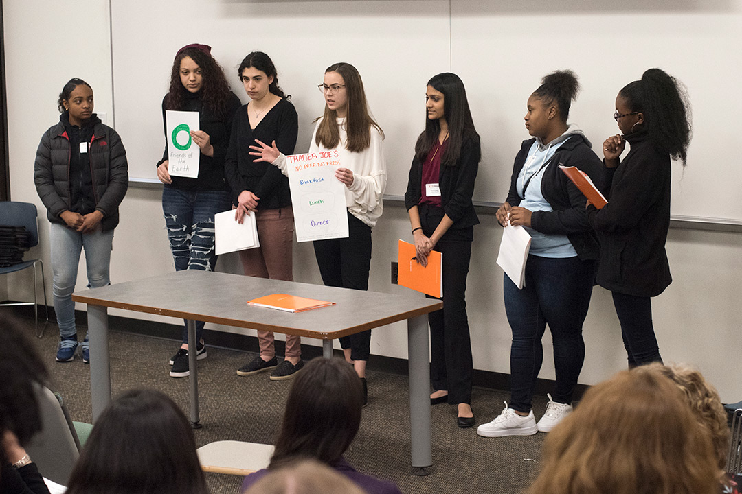 Team of high school students presents in front of group.