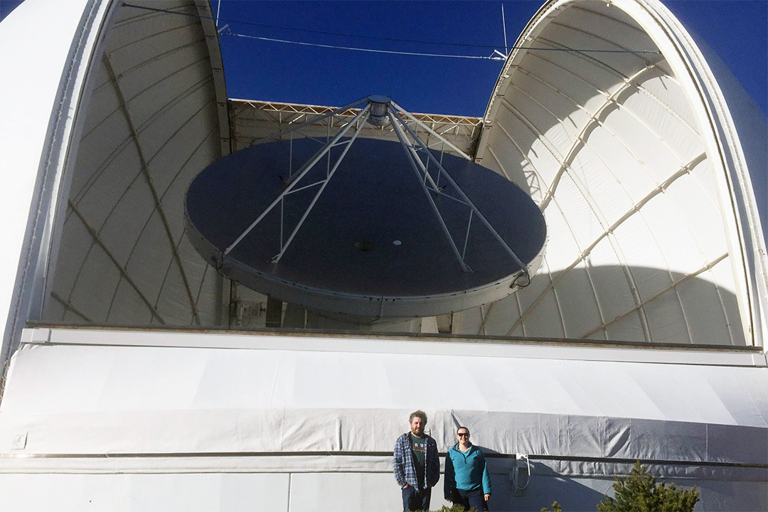 Researchers stand in front of gigantic observatory.