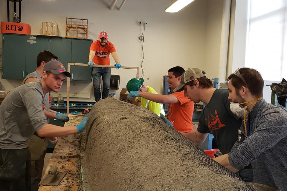 Students put concrete on wire frame of canoe body.