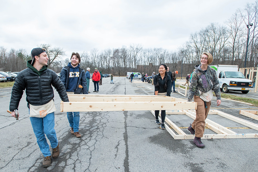 Four students walk through parking lot with wall frame.