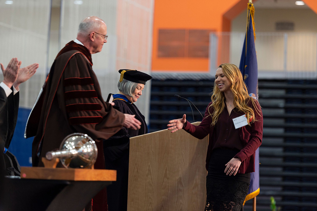Student reaches out to skae President Munson's hand while walking across a stage.