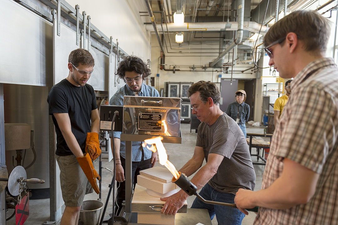 A group of artists stand around a molten glass 3D printer.