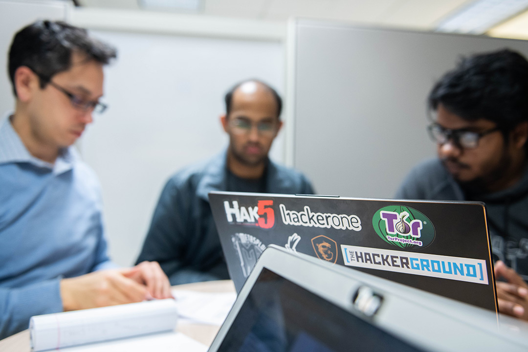 Three researchers sit at a desk on computers.