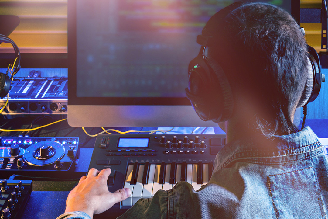 Student wearing headphones using music keyboard connected to computer monitor.