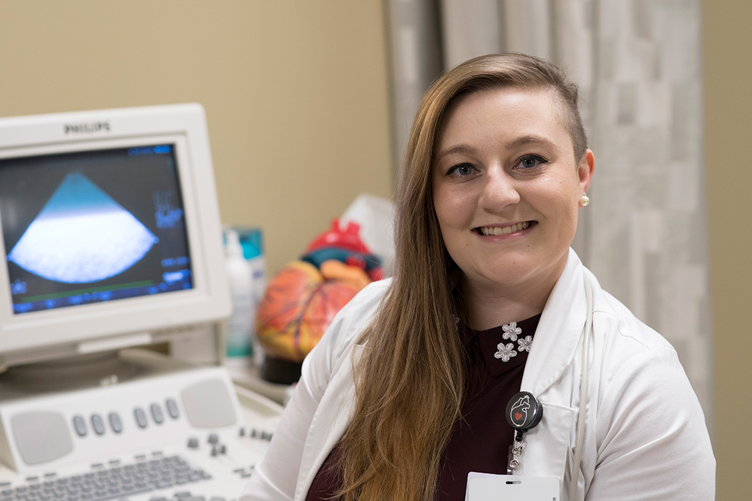 Student in lab coat in front of ultrasound machine.