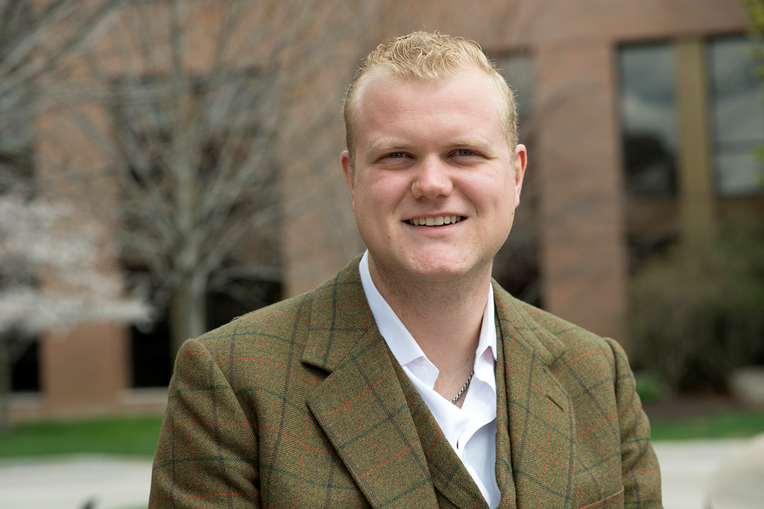 Man in plaid tweed jacket poses outside.