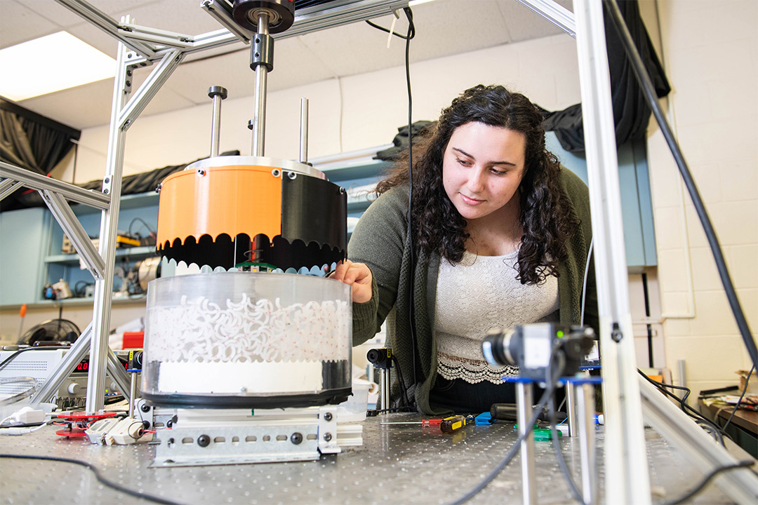 Student works on machine containing C-shaped particles.