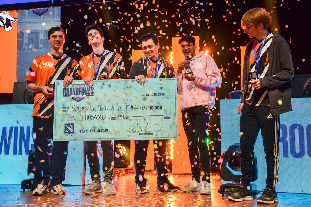 Five team members hold giant check on stage as confetti drops.