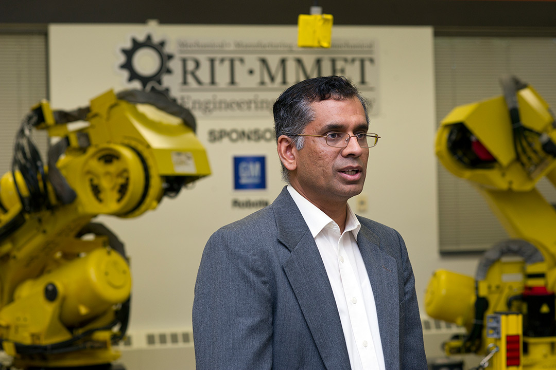 Man stands in front of yellow industrial robots.