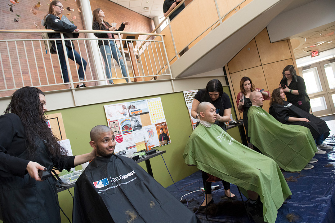 Four participants sit in barber chairs and have their heads shaved.