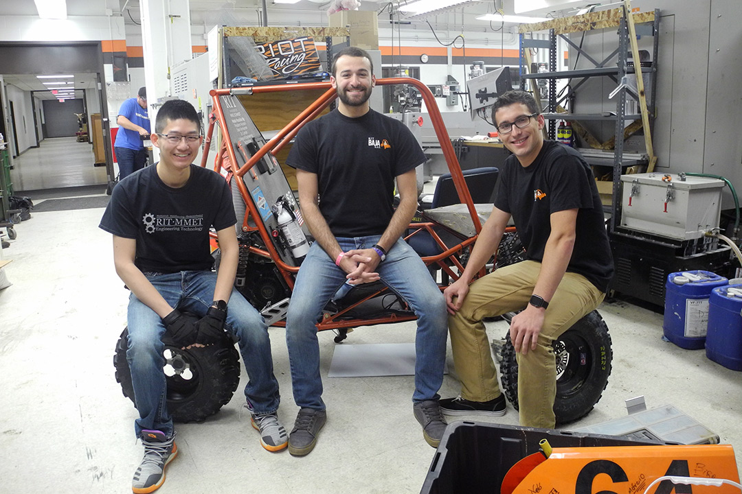 Three students sit on baja car.