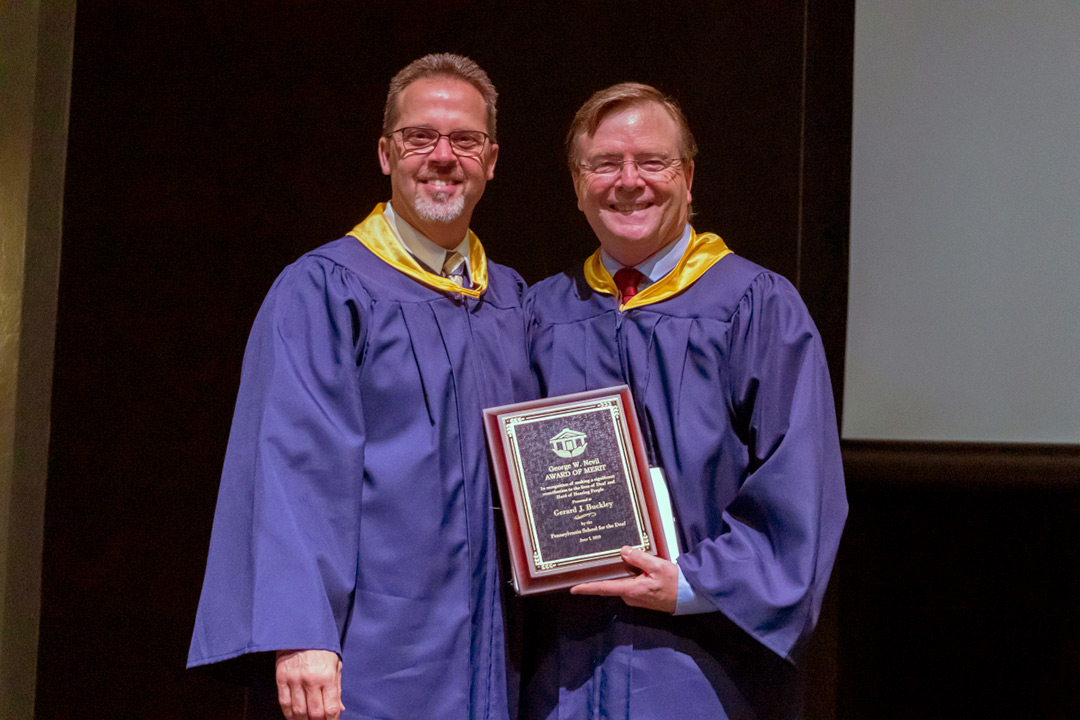 Two men wearing purple graduation robes holding plaque.