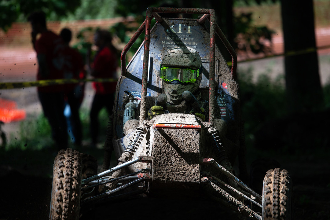 Head-on view of baja car and driver covered in mud.