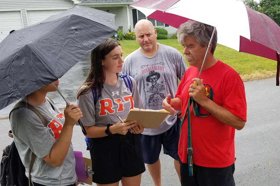 Students holding clipboard and umbrellas talk to lakeshore resident.