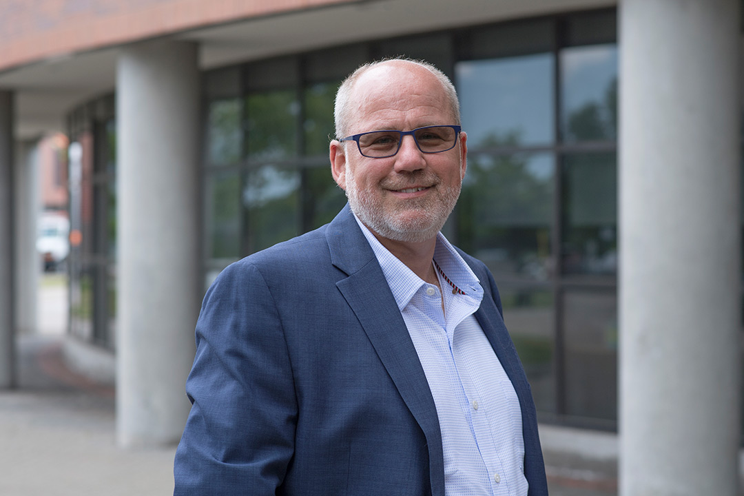 Man wearing glasses and blue suit stands outside of building.