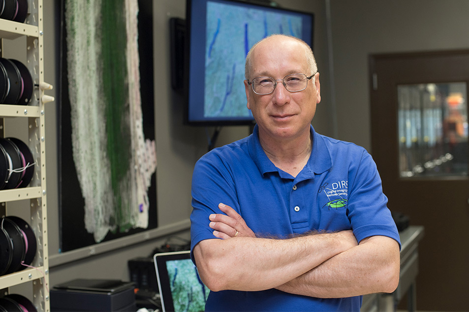 Man wearing glasses and blue polo shirt stands with arms crossed.