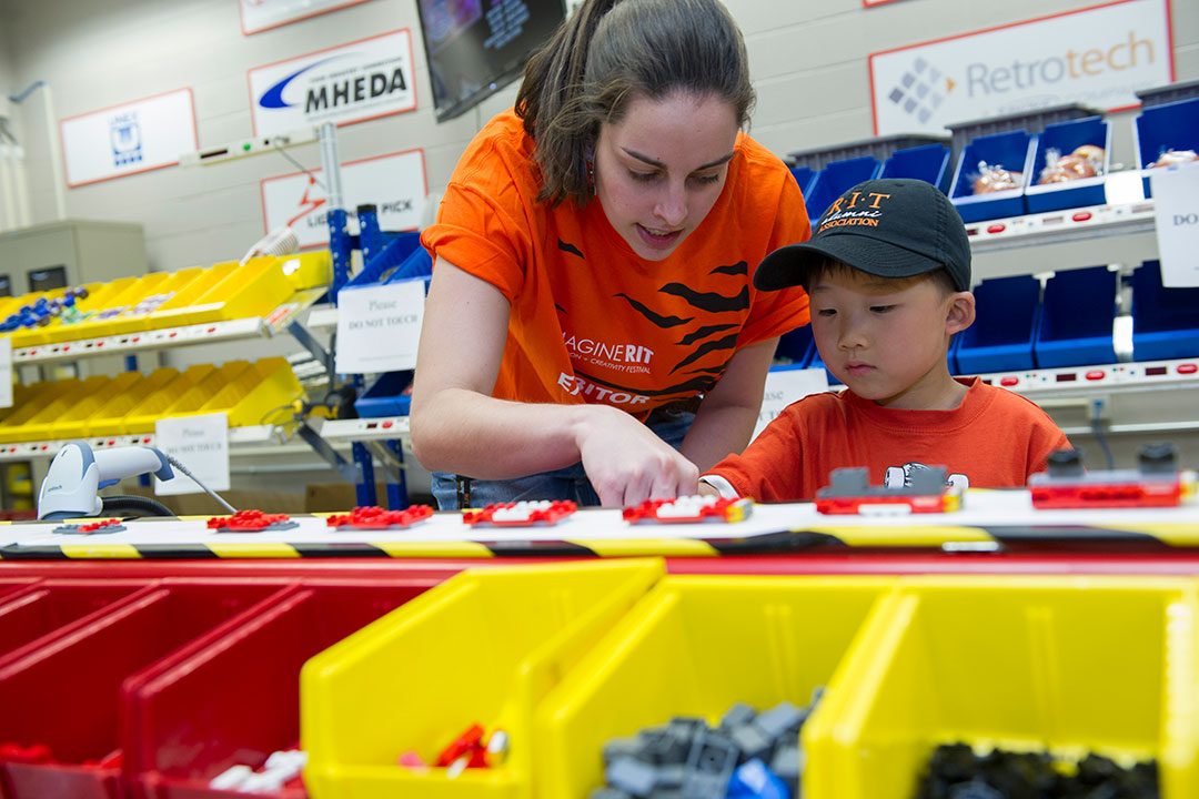 College student shows child an assembly line with Lego pieces.