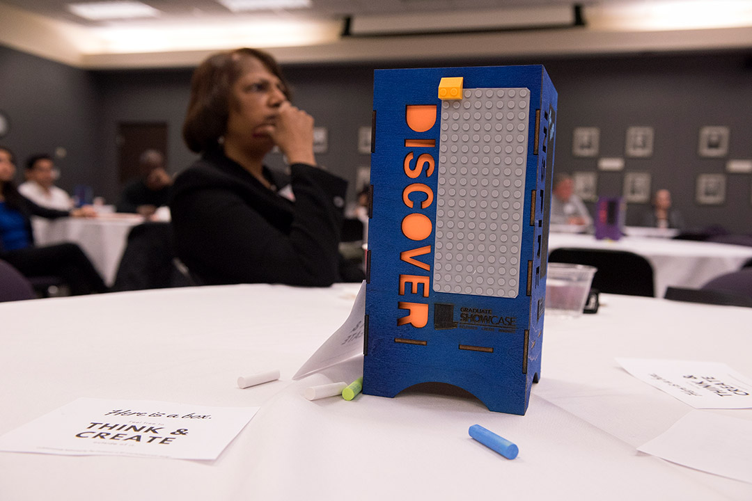 Woman sits at table with Lego structure that says Discover.