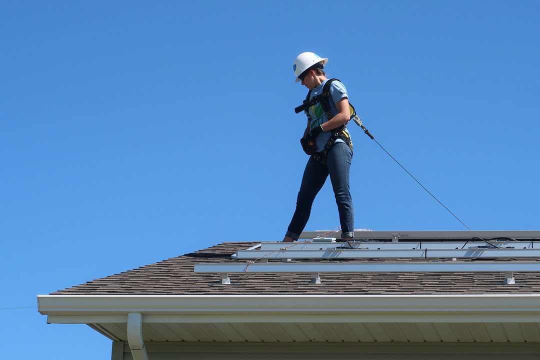 Worker wearing hardhat, harness and tether stands on roof.