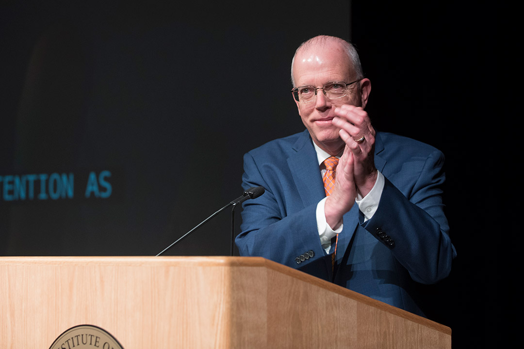 President Munson applauds at podium.