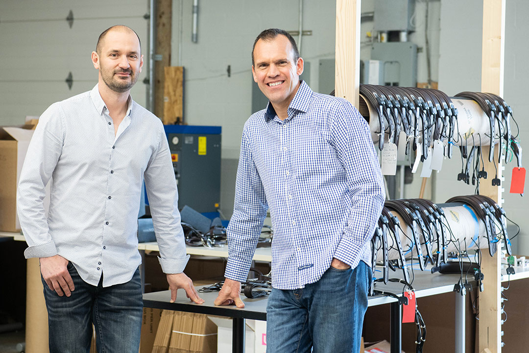 Two men pose with electronic devices for horses.