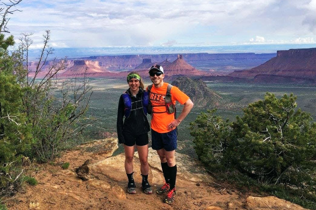 Couple in hiking gear stands on ledge with canyon in background.