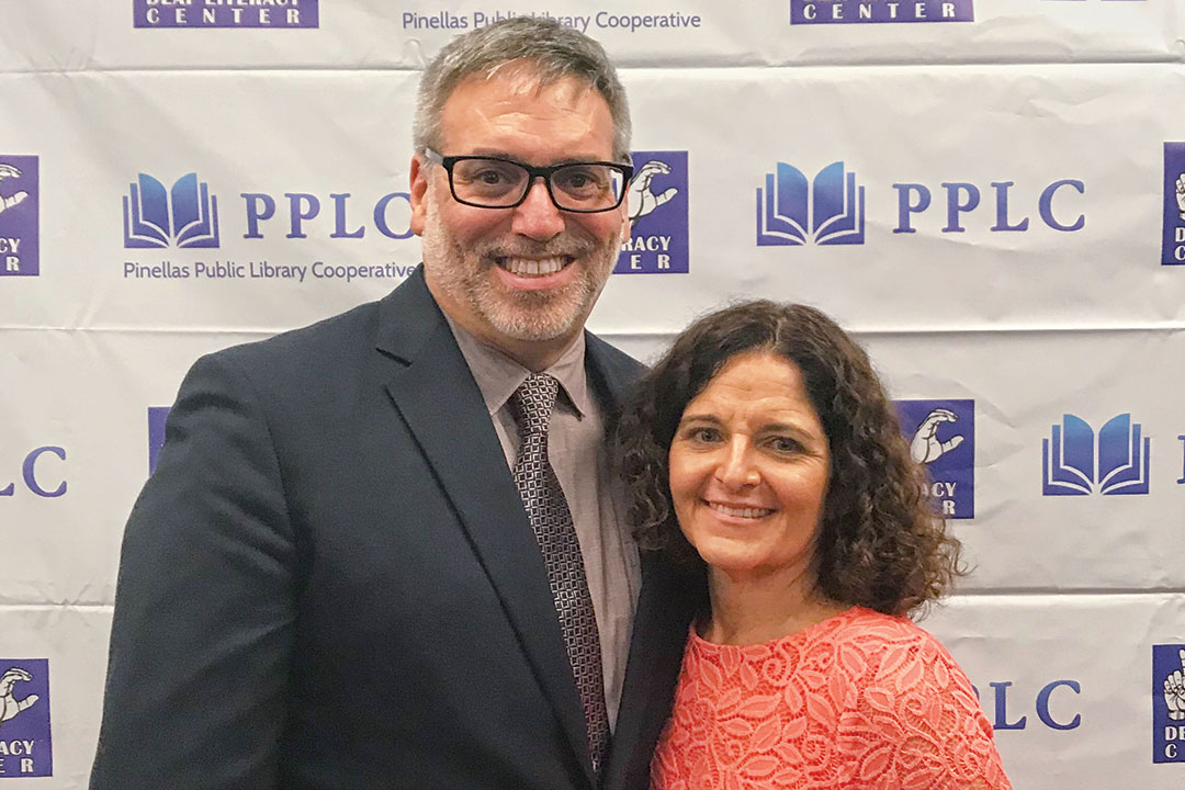 Couple stands in front of Pinellas Public Library Cooperative banner.