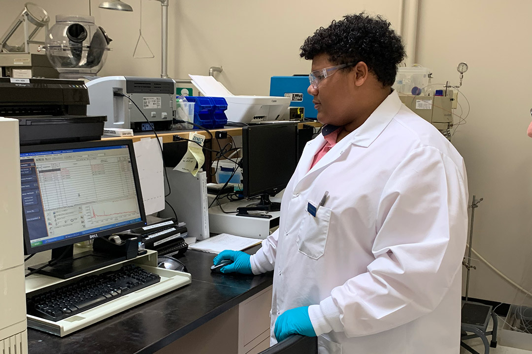 Student in lab coat works on computer.