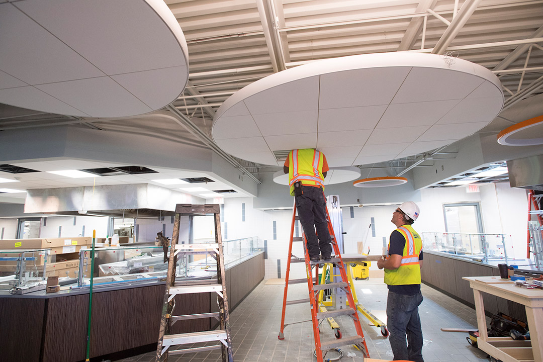 Contractors stand on ladder to work on ceiling in dining hall.