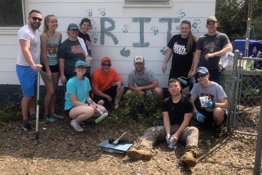 Group of students outside of house painted with the letters RIT and handprints.