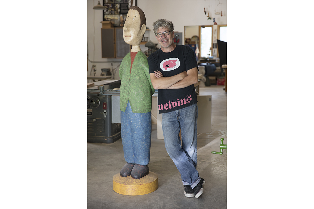 Andy Buck stands next to a wood carving of his. 