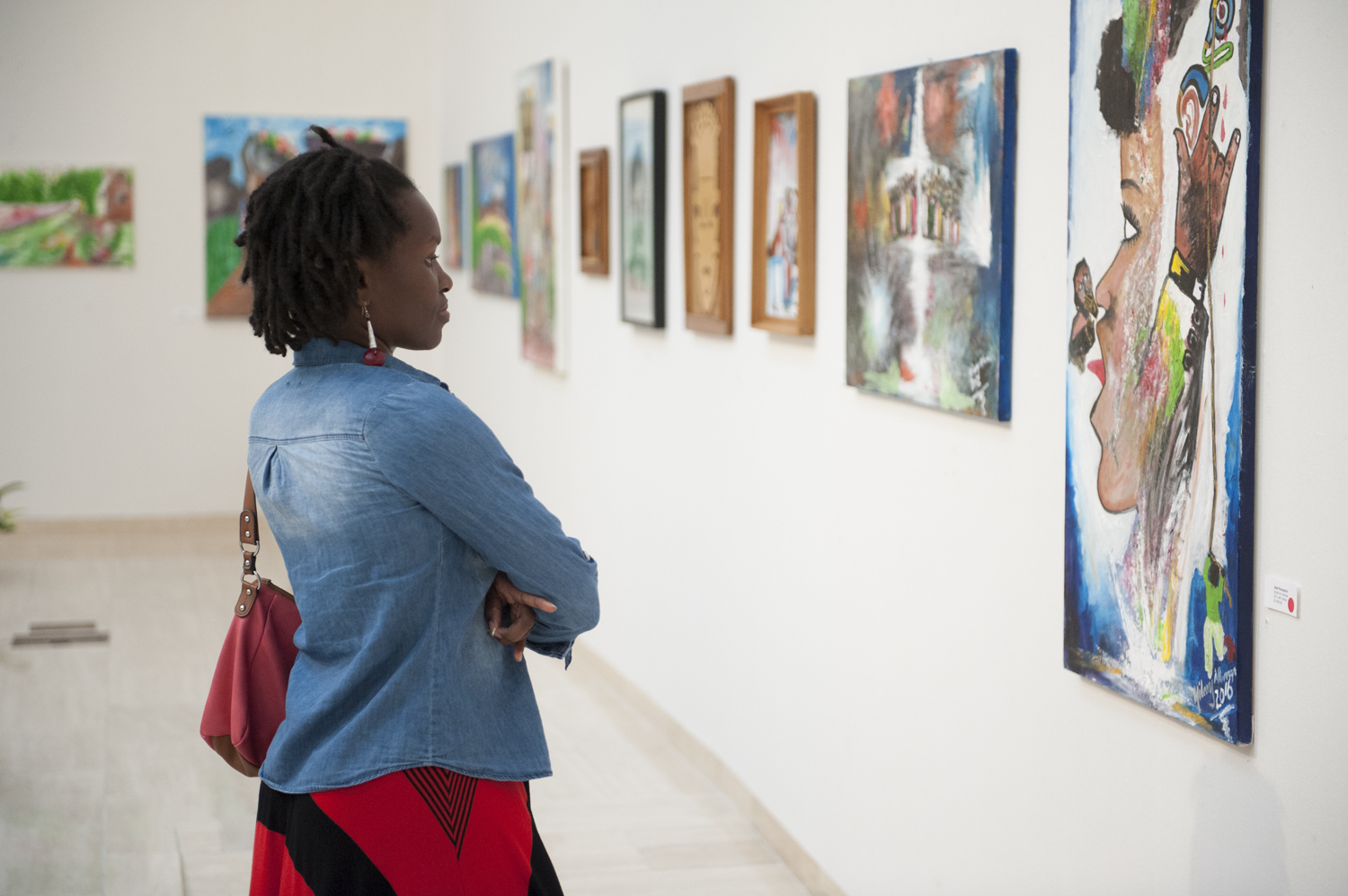 Dark-skinned female looking at colorful artwork on gallery wall.