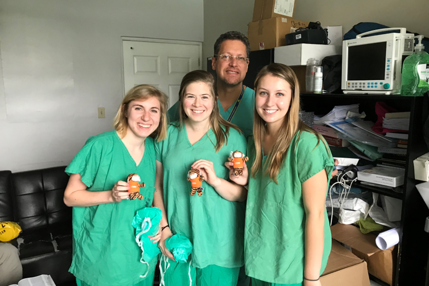 three students wearing scrubs and holding small plush tigers. 