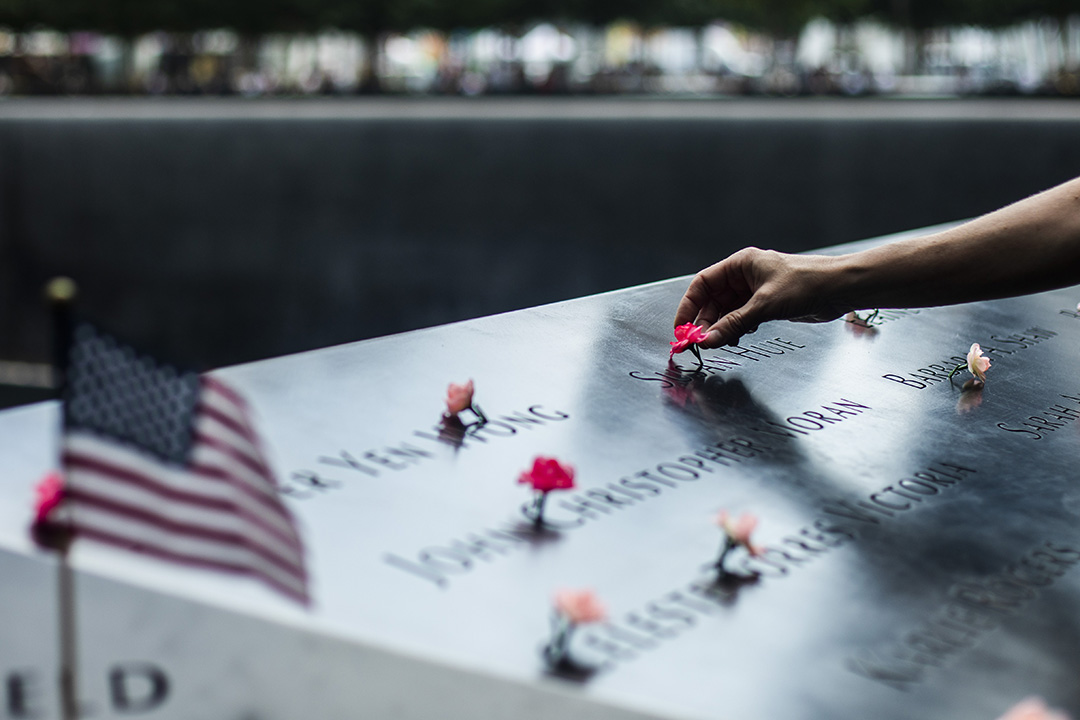 A hand touches a flower on a 9/11 memorial.
