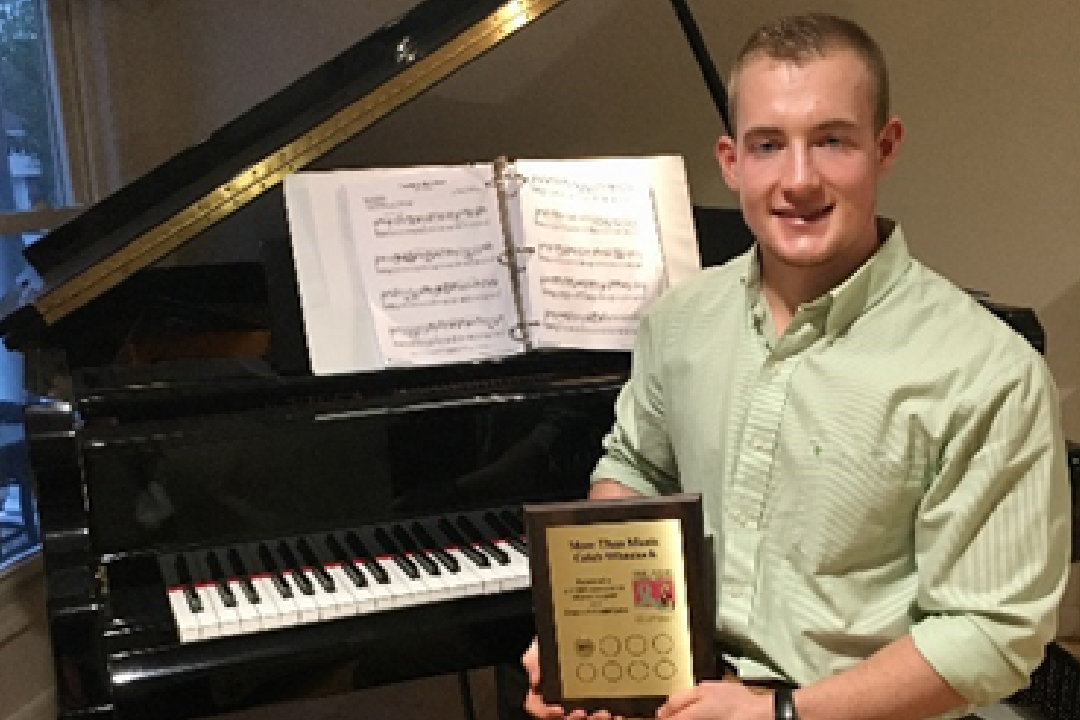 Caleb Wheelock sits in front of his piano with the plaque his nonprofit, More Than Music, earned from the Ride for Missing Children. 