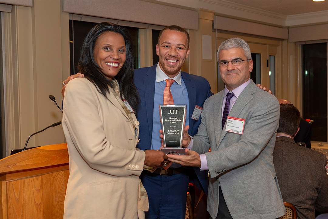 Three people stand holding award.