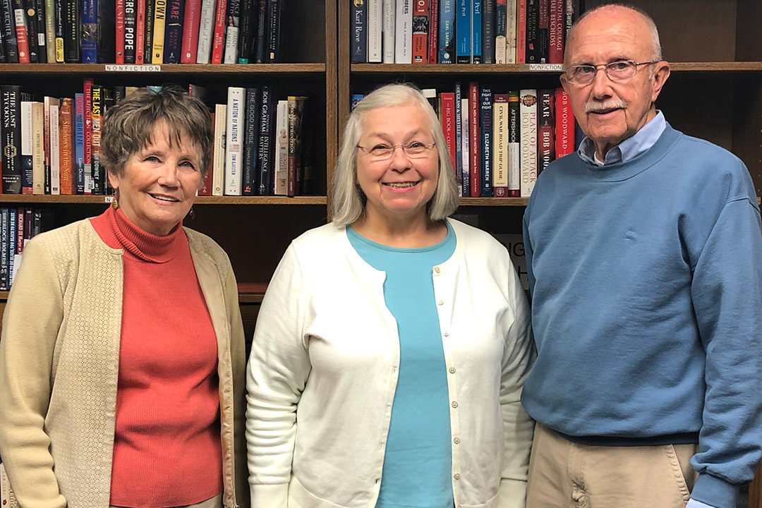 Three Osher students stand in front of bookcase.