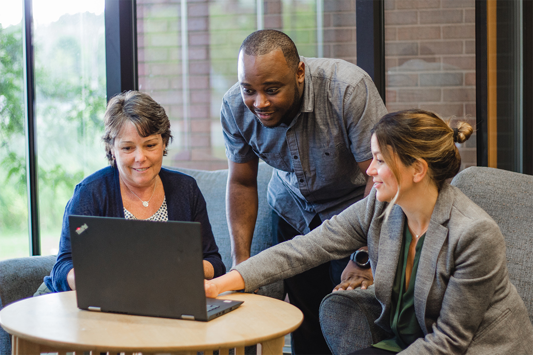 Group of three people smiling and pointing at a laptop.