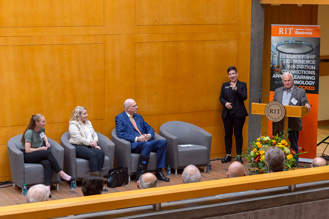 Man speaks at podium with interpreter next to him and three people seated against a wall.