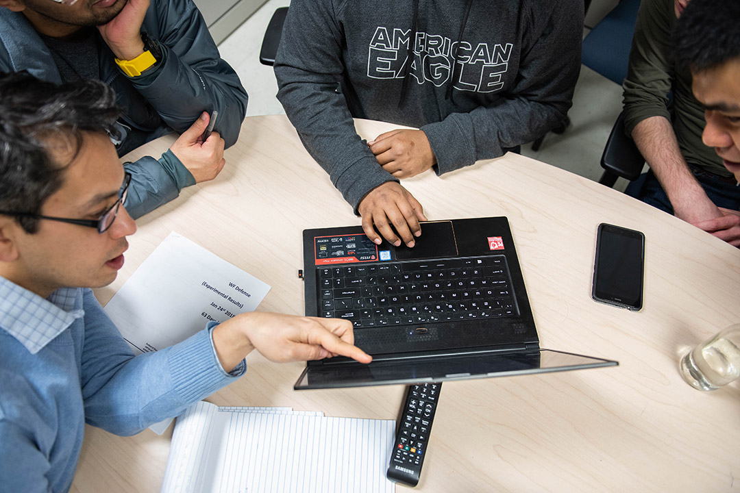 Overhead view of students and faculty member working on laptop.