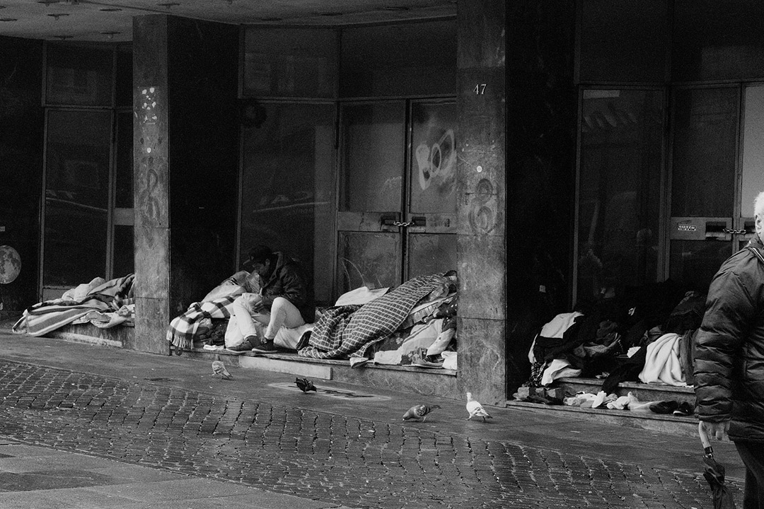 Homeless people with blankets near doors of building.